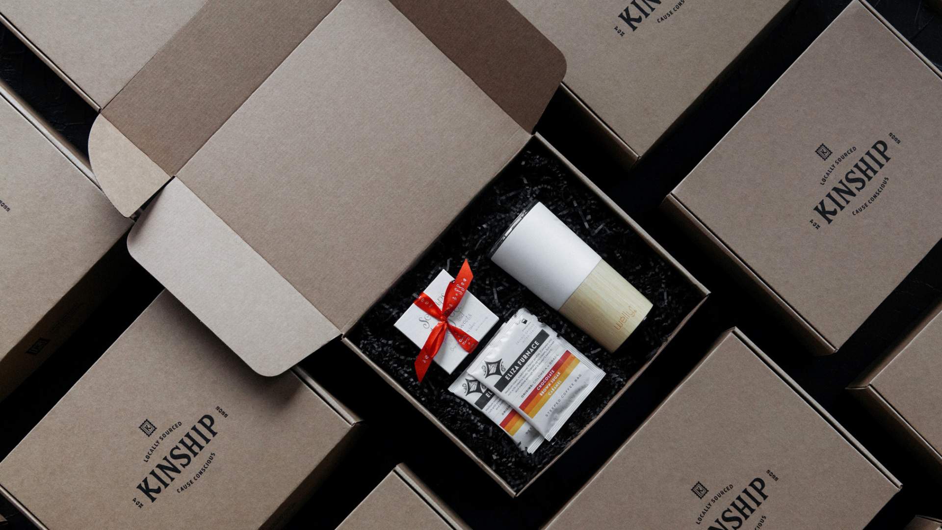 Kinship corporate gifts flatlay with closed custom packaging and one open box with Welly, De Fer Coffee, and Sacamps toffee in classic corporate gift